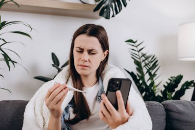 Hasta genç bayanın telefon görüşmelerini kullanarak doktor danışmanlığı ya da internet danışmanlığı ile konuşmasını kapatın evdeki oturma odasındaki kanepede oturun. Coronavirus konsepti için sosyal uzaklık, karantina