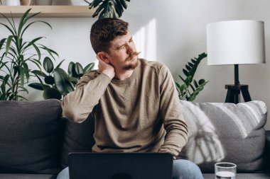 Yorgun, sakallı bir adam uzun süre evde oturarak geçirdiği işten sonra boynu ağrıyan hasta ve rahatsız hisseden. 30 'lu yaşlardaki üzgün genç adam kanepede oturup masaj yapıyor.