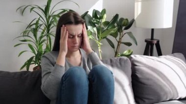 Sinir krizi, kriz konsepti. Kafasına dokunan yorgun esmer kız, baş ağrısı, migren, evdeki oturma odasında kanepede oturuyor. Depresyondaki genç kadın kayıp ve travmayla baş ediyor.