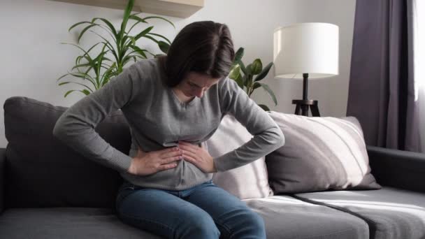 坐落于沙发上的女性因消化不良 扁桃体 腹部问题而烦躁不安 病痛的年轻妇女抱着肚子痛 肚子痛 肚子痛 胰腺炎 — 图库视频影像