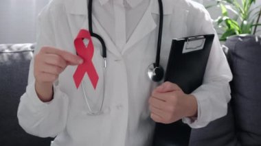 Profesyonel doktor kadın yıllık düzenli sağlık hizmetlerini destekliyor, korkunç hastalıkları olan hasta insanlara destek oluyor, sosyal AIDS kampanyası. Kadın ellerinde kırmızı kurdelenin yakın çekimi, kanser farkındalığı