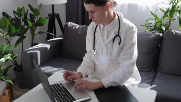 病院の机に座っているラップトップ上の白い医療均一作業に焦点を当てた若い女性医師 集中白人女性看護師またはコンピュータ画面でのGpの外観ガジェットの患者を相談 — ストック動画