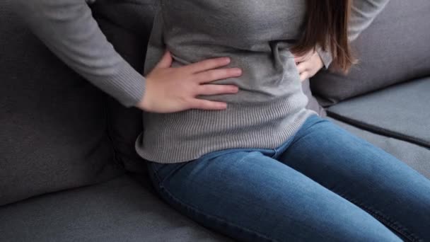 自宅のソファに座って食中毒による胃の痛みを患っている病気の若い女性の閉じる 腹部のおなかの痛みに苦しんで腹を保持している不健康な女の子 女性胃炎の健康問題 — ストック動画