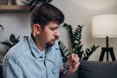 30 'lu yaşlardaki düşünceli, genç, beyaz bir adam kanepede bilgisayar başında çalışıyor. Geceleri yalnız çalışan, gözlüklü, sakallı, serbest çalışan adam. Akşamları merkez büroda çalışan uzaktan çalışan bir işçi.