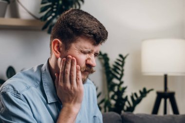 Diş ağrısı ve bakımı olan hasta bir genci yakından takip etmek rahatsızlık veriyor. Sakallı milenyumda evdeki koltukta otururken diş eti iltihabı. Diş ağrısı, diş ağrısı, diş problemi kavramı.