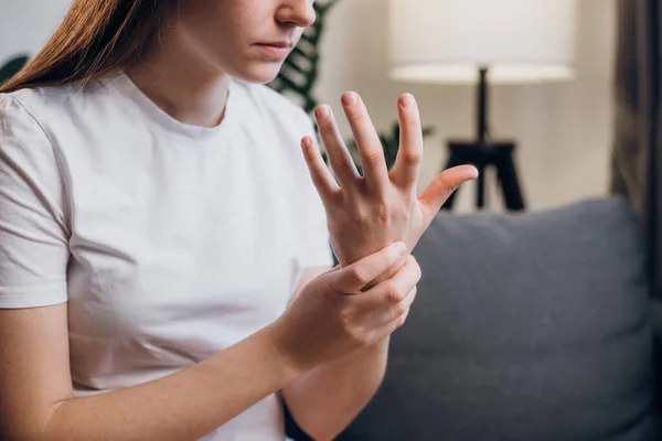 手首の痛みを持つ不健康な動揺若い白人女性は自宅のリビングルームでソファに座って苦しみを緩和しようとします 関節のある手首の女性の手のクローズアップ 手首の痛みの概念 — ストック写真