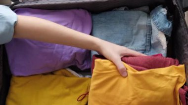 Üst görüntüde kadın elleri toplanıyor ve bavulu düzenliyor. Sıralama ve bagaj paketleme için giysi yığını. Tatile hazırım. Seyahat blogu temel gereksinimleri, yolculuk gezisi gezintisi yaşam tarzı