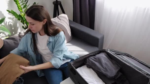 女旅行者把衣服放在舒适的沙发上 放在家里或宾馆的客厅里 航行探险准备工作 旅游妇女为度假旅行打包行李 准备旅行行李的女性 — 图库视频影像