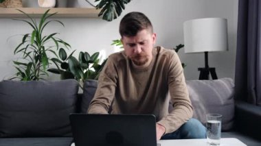 Üzgün genç adamın kanepeye oturup boynuna dokunuşunu yakından çek. Yorgun, sakallı, boynu ağrıyan bir adam. Uzun süre evde oturmaktan sonra kendini rahatsız ve rahatsız hisseden bir adam.