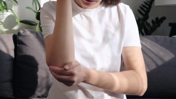 一个悲伤的年轻女人坐在沙发上 手肘酸痛 用手按摩以减轻疼痛和疼痛 不幸的女孩在家里忍受着痛苦 保健概念 — 图库视频影像