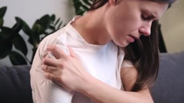 Kol yaralanması, omuz ve ön kol ağrısı, vücut kası sorunları, sağlık ve tıp konsepti olan insanlar. Üzgün genç bir kadının kanepede oturup diğer eliyle omuz omuza masaj yapmasını yakından çek.