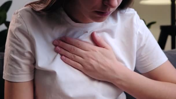 呼吸困難胸の痛み 若い不健康な女性は 心の痛みを呼吸困難ソファに座って 手で彼の胸に触れます 心臓発作 胸部骨症 パニック発作の概念 — ストック動画