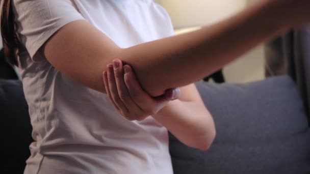 一位不健康的年轻高加索女人在清晨走近肘部 在家中坐在灰色沙发上按摩 在创伤后热身受伤的手 肘部疼痛关节炎的概念 — 图库视频影像