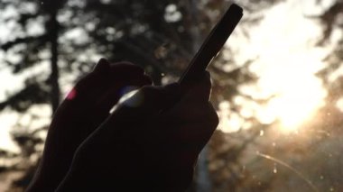 Milenyum kuşağı kadın parşömenleri telefondaki uygulamayla haberlerde yayınlanıyor. Sonbahar günbatımında arka planda akıllı telefon kullanan tanınmayan genç bir kadının yakın çekimi. Gündoğumundaki kızın sinematik görüntüsü. Telefonu kullan.