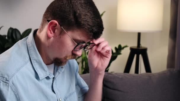 一个心事重重的年轻高加索人坐在沙发上 在电脑前工作 戴眼镜的大胡子自由职业者晚上在笔记本电脑上打字 晚上在总公司工作的远程工作者 — 图库视频影像