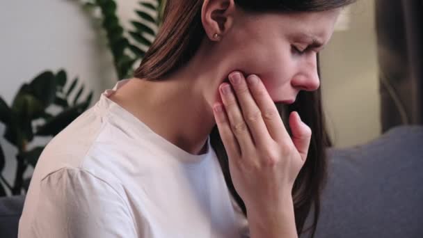 紧闭心烦意乱的年轻女子用手摸嘴 痛苦的表情因为牙病 牙医的观念 生病的黑发女子和龋牙痛坐在家里沙发上 — 图库视频影像