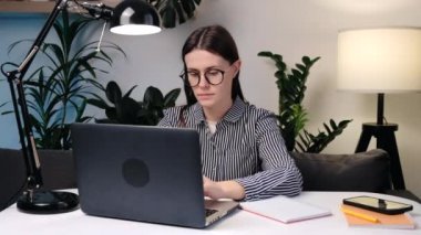 Gözlüklü üzgün genç bir kadının bilgisayar işyerindeki koltukta oturması dirsek ekleminde ağrı ve rahatsızlık hissetmesi ve acı verici bir el masajı. Eklem iltihabı, ortrosit, kemik iltihabı