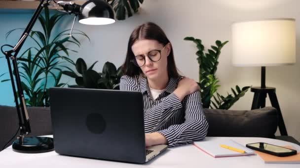 戴眼镜的年轻女人在电脑前学习到深夜 脖子都痛 女孩跪在脖子上 一边按摩一边在笔记本电脑上工作 肌肉恢复和按摩 颈部疼痛 颈椎病的概念 — 图库视频影像