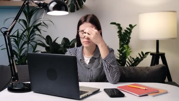 若い女性は ラップトップ上の自宅のオフィスの仕事に座って眼鏡マッサージ鼻橋を取る眼の疲れを軽減します ドライアイ レーザービジョン補正 ライフスタイル 現代のデバイスは 目の健康の概念に悪い影響 — ストック動画