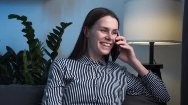 Gülümseyen esmer kadın, yurtdışındaki akrabalarıyla uluslararası gezme çağrısıyla iletişim kuruyor. Kendine güvenen genç bayan hoş bir telefon görüşmesi yapıyor. Evdeki kanepede otur.