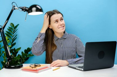 Düşünceli, sorunlu sekreter, beyaz ofis masasında çalışan 20 'li yaşlarda genç beyaz bir kız. Yan tarafa bakarken şok olmuş. Mavi stüdyo arka planında izole edilmiş bir şekilde poz veriyor. İş konsepti