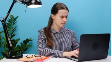 İş kadını ofis masasında oturur, bileğine dokunur, acı hisseder. Aktif ve uzun süreli klavye ve fare kullanımı nedeniyle karpal tünel sendromu olan üzgün bir kadın, mavi duvarda izole edilmiş.