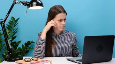 Tişörtlü genç iş kadını beyaz ofis bilgisayarında çalışıyor elinde kırmızı soru işareti işareti var. Stüdyonun mavi arka plan duvarında izole edilmiş duruyor. İş konsepti