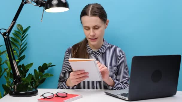 従業員の笑顔ビジネス女性ノートブックにメモを書く毎日プランナー 計画週 仕事や勉強 ノートパソコンを使用して 美しい女性のリスニングの講義を 青の背景の壁に隔離ポーズ — ストック動画