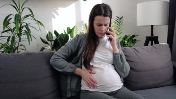 靠近不快乐的高加索年轻孕妇 坐在客厅的沙发上 摸着肚子 生儿育女 生儿育女和待在家里 — 图库视频影像