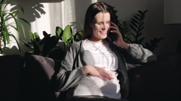 积极放松的年轻漂亮孕妇 大肚子 在舒适的沙发上悠闲自在地呆在家里 与家人进行愉快的长途电话交谈 与家人分享消息 讨论分娩 — 图库视频影像