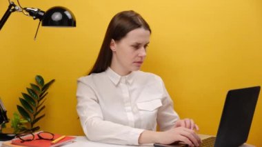 Portrait of strict employee business woman in white shirt sit work at office desk with laptop do point index finger camera on you command, posing isolated over yellow color background wall in studio