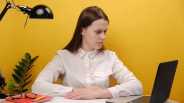 Portrait of employee business woman in shirt sit work at office desk pc laptop holding sad face, bad emoticon, posing isolated over yellow color background wall in studio. Achievement career concept