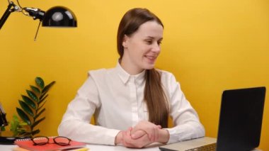 Successful employee business woman sit work at office desk with pc laptop make conference online call, smiling young girl user waving hand doing internet video chat, posing on yellow background wall