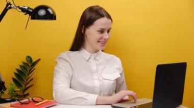 Portrait of happy young employee businesswoman sitting at workplace with laptop and showing big white hashtag symbol, sharing viral content, tagged message, posing isolated over yellow background wall