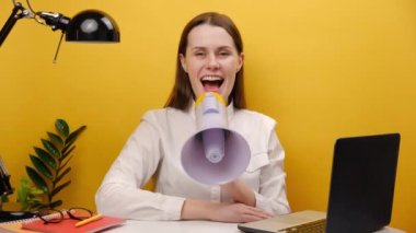 Attractive employee young business woman 20s sitting work at white office desk laptop holding scream megaphone announces discounts sale Hurry up, posing isolated over yellow color background in studio