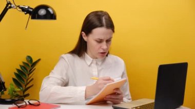 Concentrated young businesswoman working on computer and types sit at office desk, communicating with clients, isolated on yellow background wall. Girl international company employee busy with project