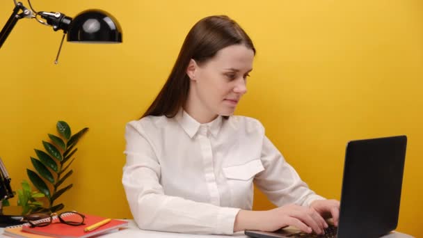 秘密の成功した従業員の肖像画ビジネス女性20代の白いシャツでオフィスデスクで仕事に座るノートパソコンと言う急いで静かに指で唇Shhジェスチャー 黄色の背景スタジオ上にポーズ — ストック動画