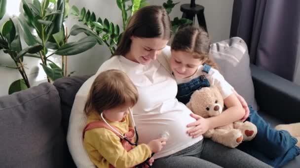 Playful Cute Little Daughters Using Medical Stethoscope Listening Pregnant Mom — Video