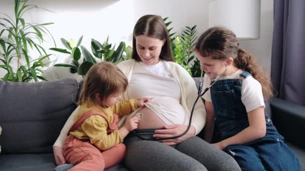 Χαριτωμένες Δύο Μικρές Κόρες Εφαρμογή Στηθοσκόπιο Έγκυο Κοιλιά Μαμά Ακούγοντας — Αρχείο Βίντεο