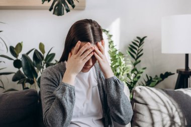 Worried young woman think of overcoming bad life event ponder on hard decision. Critical situation concept. Sad female sitting on sofa lean forward on folded hands try to keep emotions under control