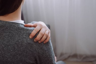 Close up back view of unhealthy young caucasian woman touching painful shoulder feeling discomfort sitting on couch at home. Copy space for promotion content. Injuries Poor health Illness concept