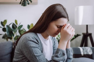 Close up of concerned sad young woman sitting on couch at home thinking of problem looks in distance feels depressed due loneliness, inner emptiness, life troubles, break up. Marriage split concept