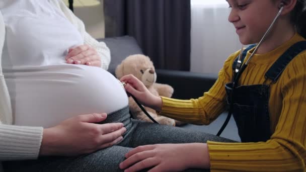Close Cute Little Daughter Plays Doctor Pregnant Mother Sit Sofa — Stok video