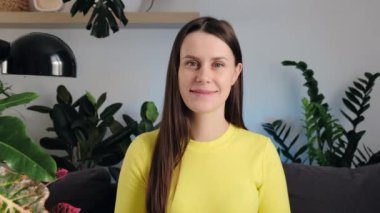 Güzel mutlu bir kadının portresi göz kırpıyor. 20 'li yaşlardaki esmer, pozitif gülümseyen kız kameraya bakıyor ve oturma odasındaki rahat koltukta gözleriyle göz kırpıyor. İnsanların duygu kavramı