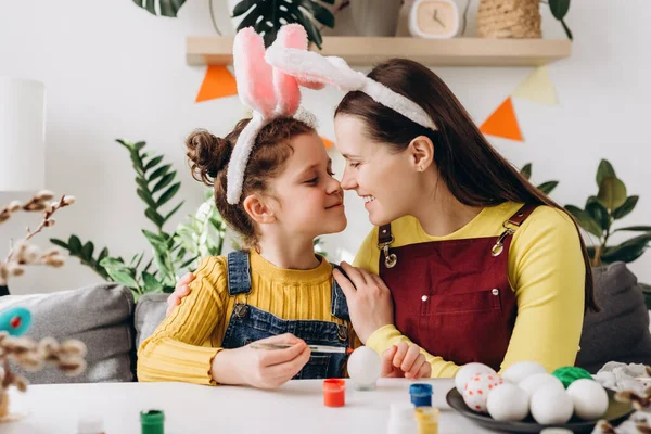 Close up of sweet family portrait of happy mother and little daughter holding painted multi-colored Easter eggs, mom with kid hugging tenderly embracing and smiling in cozy light cozy room at home