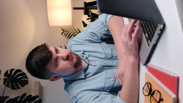 ノートパソコンに入力して研究を行う焦点を当てたビジネスマン起業家の垂直ビデオ 忙しい労働者のフリーランスは 現代の技術ノートブックデバイスに取り組んでいます コンピュータを使用してひげを生やした男は自宅のオフィスの机に座る — ストック動画