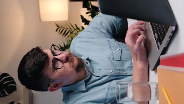 ノートパソコンで働く眼鏡の若い男の垂直ビデオは フリーランスのリモートジョブのテキストメッセージは 休憩を取る飲料天然ミネラルウォーターは 健康を気に飲み物になります 日常生活の概念 — ストック動画