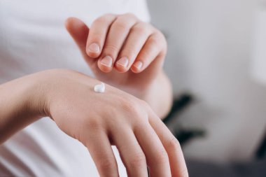 El derisine krem sürerek, doğal güzelliğin ve nemlendirilmiş sağlıklı nemlendirilmiş cilt bakımının tadını çıkaran tanınmamış genç beyaz bir kadın. Kadın elinin bakımı. Tıbbi konsept
