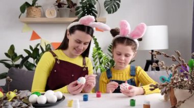 Paskalya Ailesi gelenekleri. Komik bir anne ve küçük mutlu bir kız çocuğu Paskalya bayramı için yumurtaları boyayla süslüyor, hey oyna, gül ve evdeki rahat odada otururken yüzlerini çiz.