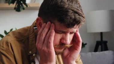 Evdeki bir kanepede oturan, yorgun, yorgun, yorgun, kişisel sıkıntılar, endişe konsepti, migren ağrısı çeken 30 'lu yaşlarda, yorgun ve bitkin bir beyaz adamın yakın çekimi.